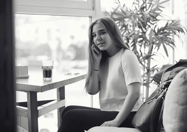 Una chica joven en un café. La chica está sentada en el sofá y hablando —  Fotos de Stock