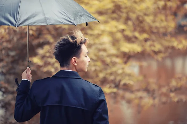 Sonbahar yağmurlu hava ve bir şemsiye ile genç bir adam — Stok fotoğraf