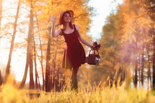 A girl in a hat on a walk in the park. A girl with a basket walks in autumn. Girl is walking along the road at sunset