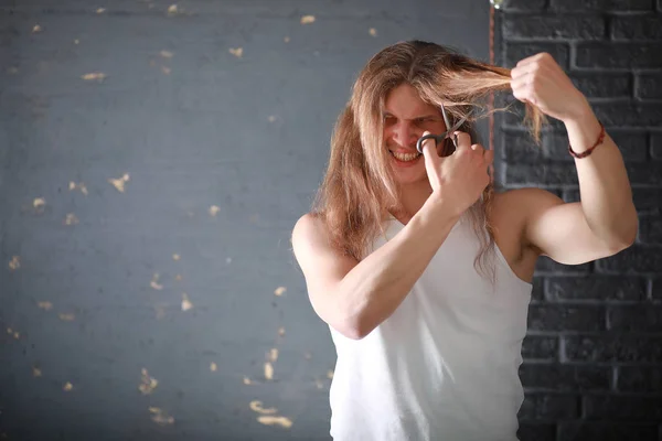 A young man with long hair cut a lock