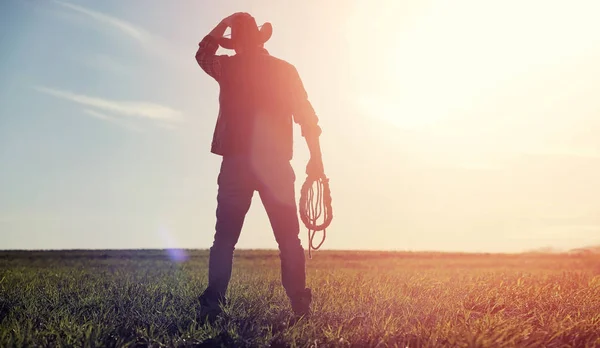 En man cowboyhatt och en loso i fältet. Amerikansk jordbrukare i ett f — Stockfoto