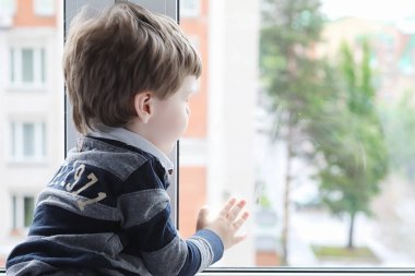 Küçük çocuk bir kitap okuyor. Çocuğun pencerenin önünde oturur bir