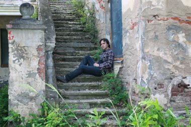 Adam terk edilmiş merdivenlerde oturuyor.