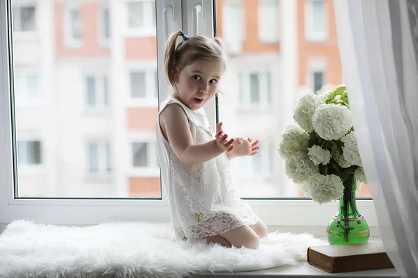 小さな女の子は、窓辺に座っています。花の花束 — ストック写真