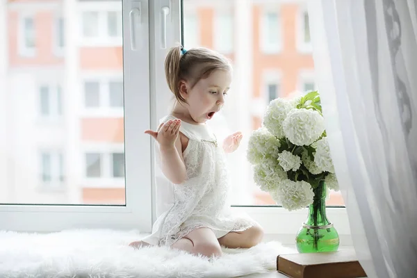 小さな女の子は、窓辺に座っています。花の花束 — ストック写真