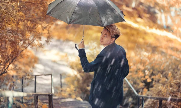 Herbstliches Regenwetter und ein junger Mann mit Regenschirm — Stockfoto