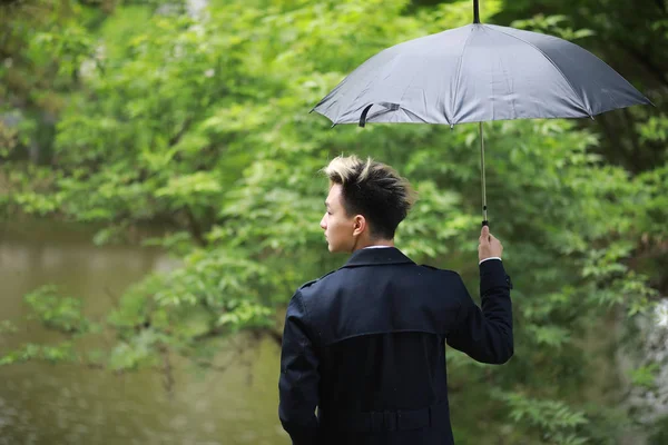 Frühlingshaftes Regenwetter und ein junger Mann mit Regenschirm — Stockfoto