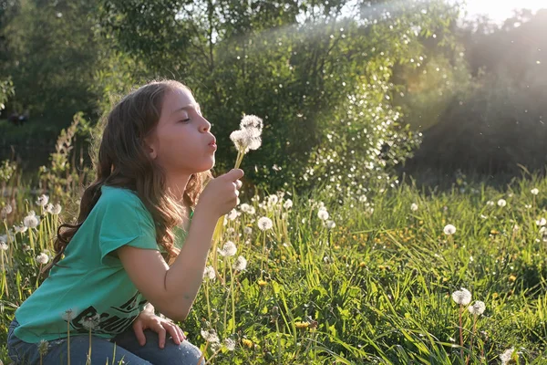 Teen blowing seeds from a dandelion flower in a spring park — Stock Photo, Image