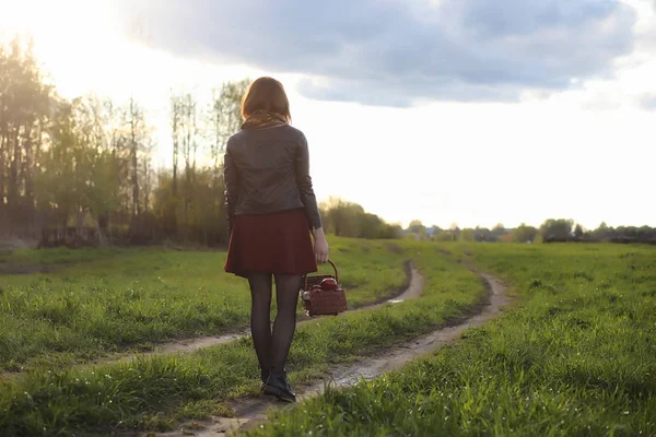 A girl in a hat on a walk in the park. A girl with a basket walks in the spring. Girl is walking along the road at sunset