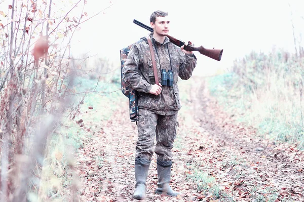 En man i kamouflage och med ett jaktgevär i en skog på en sp — Stockfoto