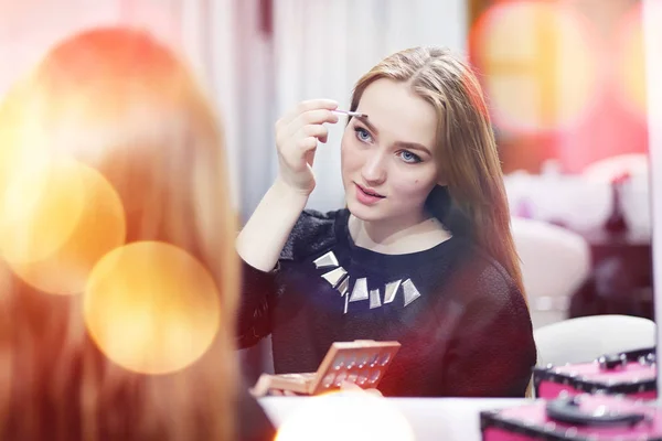 En ung pige gør make-up i en skønhedssalon. Pigen foran o - Stock-foto