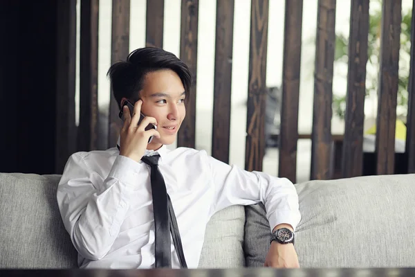 A young Asian businessman is waiting for a partner in a cafe. A Korean young man talking on the phone in a cafe