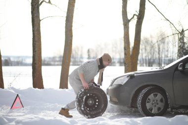 Bir adamın yanında bir kış gününde kırık bir araba