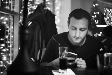 Bir gece kulübünde elinde nargile piposu ve sigara tutan bir adam. 