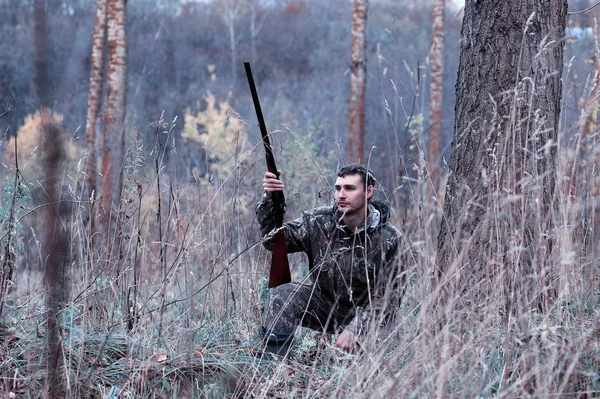 Un hombre en camuflaje y con un rifle de caza en un bosque en una sp —  Fotos de Stock