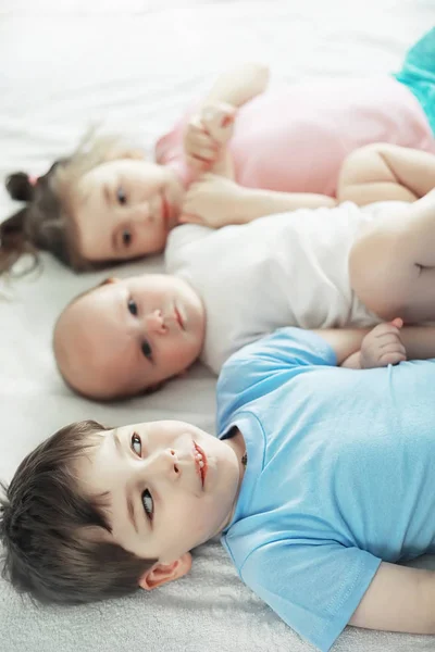 Los niños se acuestan en la cama junto al bebé recién nacido, hermanita . — Foto de Stock