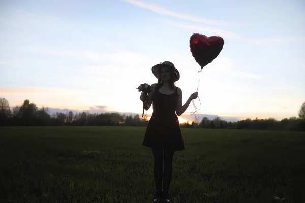 A girl in a hat on a walk in the park. A girl with a basket walks in the spring. Girl is walking along the road at sunset