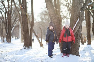Kış parkında oynayan kalın elbiseli şirin çocuklar. 