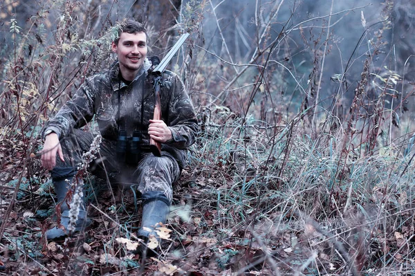 Un homme en camouflage et avec un fusil de chasse dans une forêt sur une espèce — Photo
