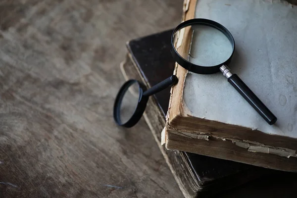 Old books on a wooden table and magnifier — Stock Photo, Image