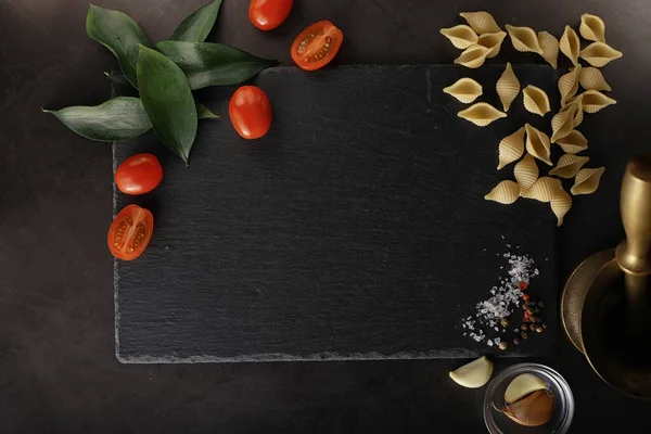 Cáscaras de pasta sobre piedra negra. Tomates y hojas de laurel con allspi — Foto de Stock