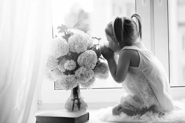 Une petite fille est assise sur le rebord de la fenêtre. Un bouquet de fleurs — Photo