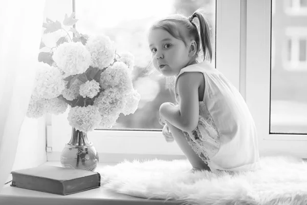 Una niña está sentada en el alféizar de la ventana. Un ramo de flores —  Fotos de Stock