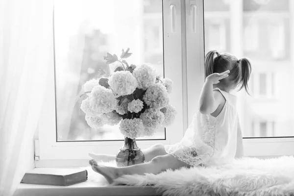 Una niña está sentada en el alféizar de la ventana. Un ramo de flores — Foto de Stock