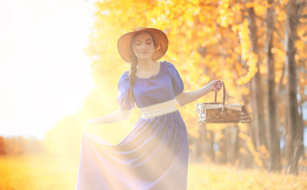 Young beautiful girl in dresses on nature. A girl in a hat walks in the park. Young woman on picnic with a basket outside the city