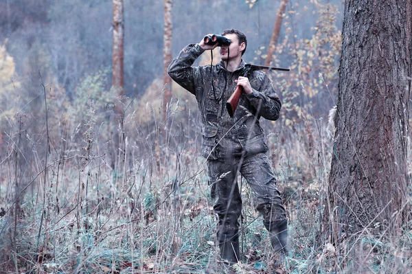 Un hombre en camuflaje y con un rifle de caza en un bosque en una sp —  Fotos de Stock