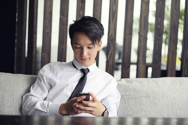 A young Asian businessman is waiting for a partner in a cafe. Bu — Stock Photo, Image