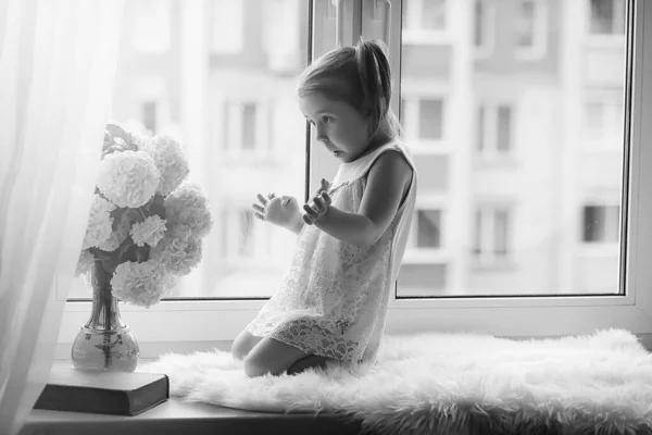 一个小女孩正坐在窗台上。一束鲜花 — 图库照片