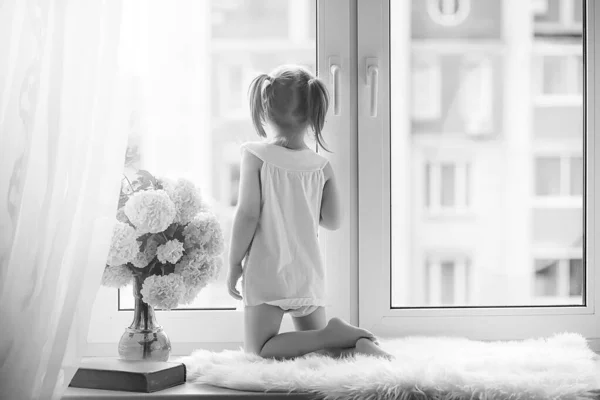 Une petite fille est assise sur le rebord de la fenêtre. Un bouquet de fleurs — Photo