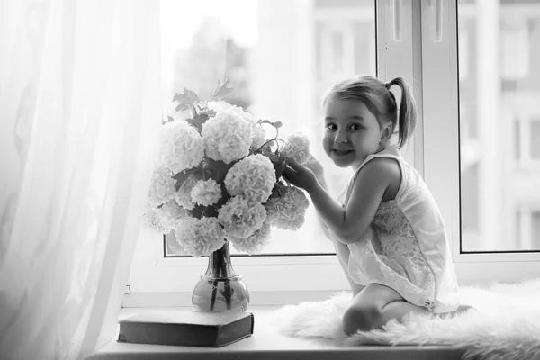 Una niña está sentada en el alféizar de la ventana. Un ramo de flores —  Fotos de Stock