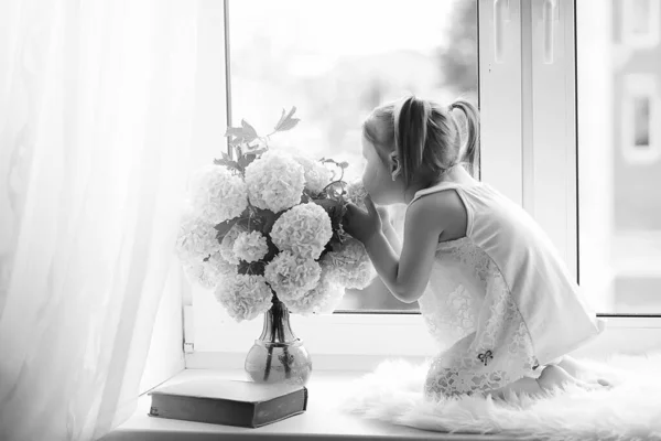 Una niña está sentada en el alféizar de la ventana. Un ramo de flores —  Fotos de Stock