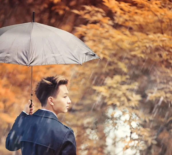 Autunno tempo piovoso e un giovane uomo con un ombrello — Foto Stock