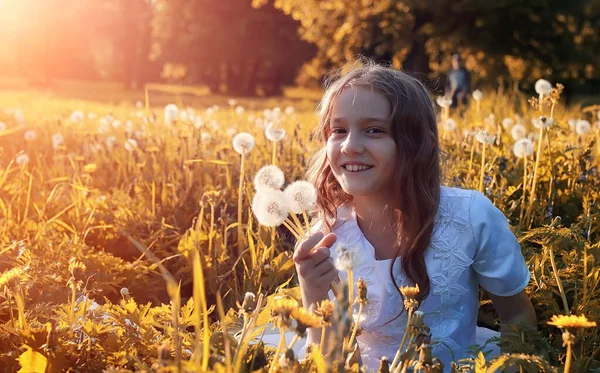 Teen blowing seeds from a dandelion flower in a park — Stock Photo, Image