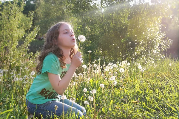 Teen blowing seeds from a dandelion flower in a spring park — Stock Photo, Image