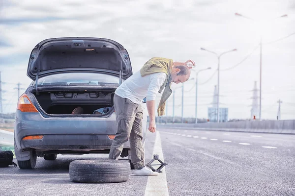 Ersätter hjulet på en bil på vägen. En man som utför däckarbete — Stockfoto