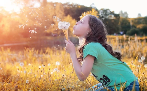 Teen blowing seeds from a dandelion flower in a park — Stock Photo, Image