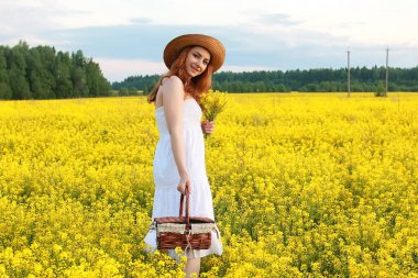 Sarı çiçekli bir tarlada saman şapkalı kız çiçek açıyor.