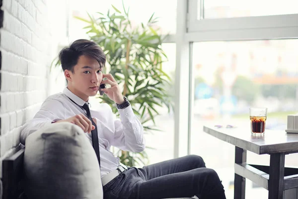 En ung asiatisk affärsman väntar en partner i ett café. Bu — Stockfoto