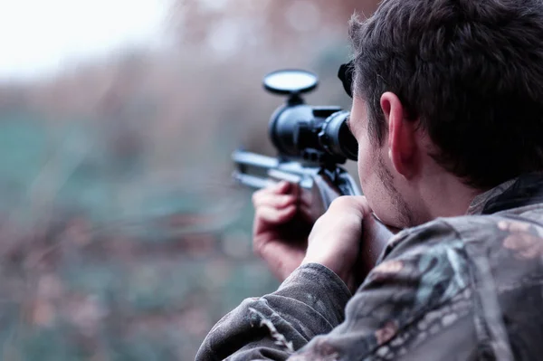 Un hombre en camuflaje y con un rifle de caza en un bosque en una sp — Foto de Stock