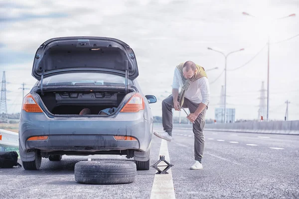 道路上の車のホイールを交換します。タイヤの仕事をしてる男 — ストック写真