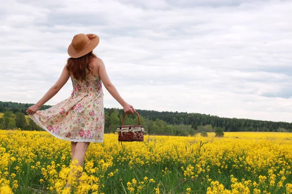 Menina em um campo de flores com cesta e um chapéu — Fotografia de Stock