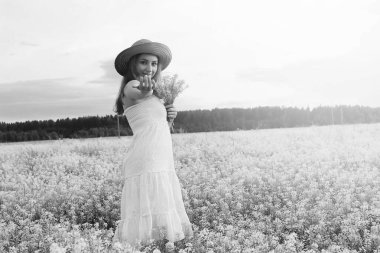 şapkalı genç kızın tek renkli resmi büyük bir çiçek tarlasında duruyor.