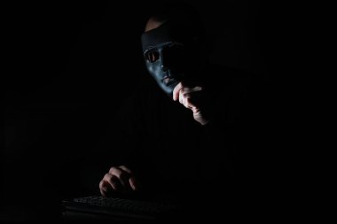 Maskeli bir adam karanlıkta klavyeye baskı yapmış.