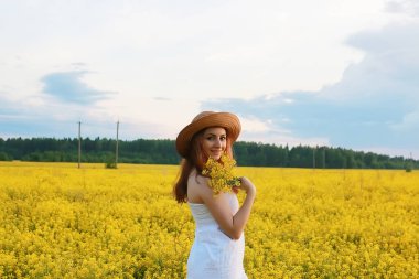 Sarı çiçekli bir tarlada saman şapkalı kız çiçek açıyor.