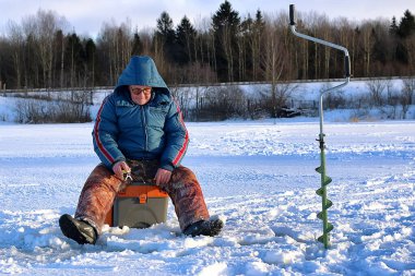 Yaşlı adam kışın gölde balık tutuyor.