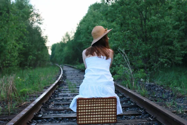 Ragazza in un sundress bianco e valigia di vimini che cammina su rotaie — Foto Stock